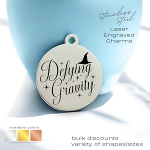 May include: A silver charm with the text "Defying Gravity" and a witch's hat. The charm is laser engraved and available in a variety of colors.