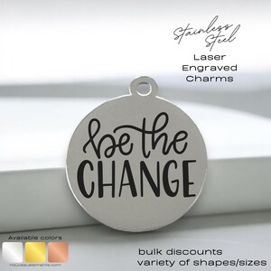 May include: A silver round charm with the words "be the CHANGE" engraved in black lettering. The charm is made of stainless steel and is available in a variety of colors.