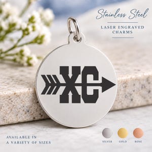May include: A round silver-colored stainless steel charm featuring a laser-engraved black graphic of the letters XC intersected by an arrow. The charm includes a small metal jump ring at the top for attachment. Text on the image reads Stainless Steel.