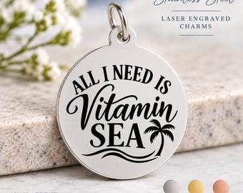 May include: A circular stainless steel charm featuring a laser-engraved design with the text ALL I NEED IS Vitamin SEA and a palm tree graphic. The charm includes a jump ring at the top and is available in silver, gold, and rose metal finishes.