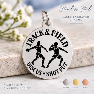 May include: A round stainless steel charm featuring a laser-engraved black graphic of two athletes, one throwing a discus and one performing a shot put. The text reads TRACK & FIELD, DISCUS, and SHOT PUT. The charm includes a silver jump ring.