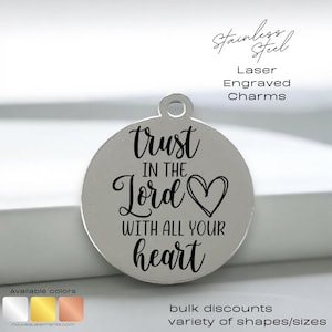 May include: A silver round charm with the words "trust in the Lord with all your heart" engraved on it. The charm has a small heart symbol next to the word "Lord".
