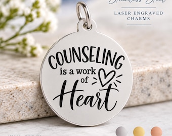 Könnte beinhalten: Ein runder, silberfarbener Edelstahl-Anhänger mit einem Biegering. Der Anhänger ist mit dem schwarzen, lasergravierten Text "COUNSELING is a work of Heart" und einem kleinen Herzsymbol versehen. Der Text "Stainless Steel LASER ENGRAVED CHARMS" ist sichtbar.