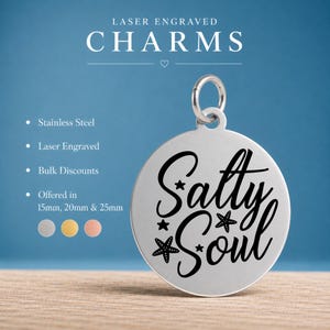 May include: A round stainless steel charm with a silver finish featuring the laser engraved text Salty Soul in a black script font, accented with small star and starfish icons. The charm includes a jump ring at the top for attachment purposes.