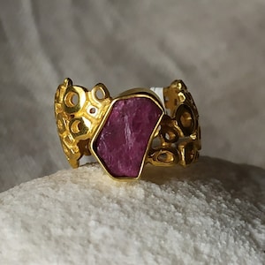Puede incluir: Un anillo de oro con una gran piedra preciosa de rubí rosa facetada engastada en un diseño decorativo intrincado.
