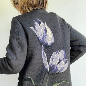 Puede incluir: Una chaqueta negra con un diseño floral con dos tulipanes morados con tallos y hojas verdes.
