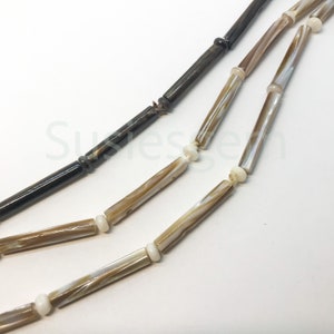 May include: A multi-strand necklace made of brown and white shell beads. The beads are long and cylindrical, and they are strung together on a thin cord. The necklace is a simple and elegant design.