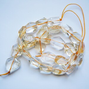 May include: A strand of clear quartz beads with a golden hue, strung on a thin orange thread. The beads are faceted and have a geometric shape.