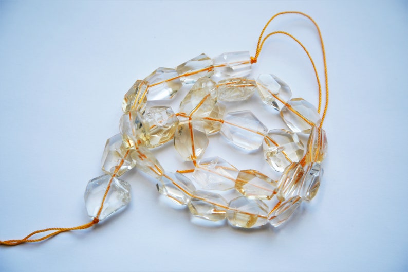 May include: A strand of clear quartz beads with a golden hue, strung on a thin orange thread. The beads are faceted and have a geometric shape.