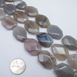 May include: A strand of gray, white, and brown agate beads. The beads are faceted and have a slightly irregular shape. The beads are about 1 inch long and 1/2 inch wide. The beads are strung on a clear elastic cord.