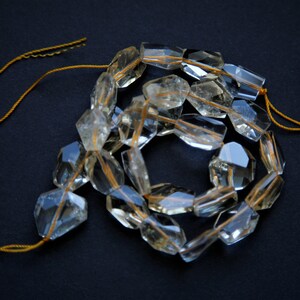 May include: A strand of clear quartz beads with a golden thread running through each bead. The beads are faceted and have a slightly yellow hue. The beads are strung on a gold cord.