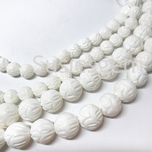 May include: A strand of white carved shell beads. The beads are round and have a floral design. The beads are strung on a white cord.