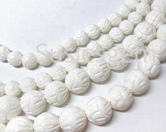 Puede incluir: Una hebra de cuentas de concha talladas blancas. Las cuentas son redondas y tienen un diseño floral. Las cuentas están enhebradas en un cordón blanco.