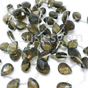 May include: A strand of dark green gemstone beads in a teardrop shape. The beads are strung on clear elastic thread.