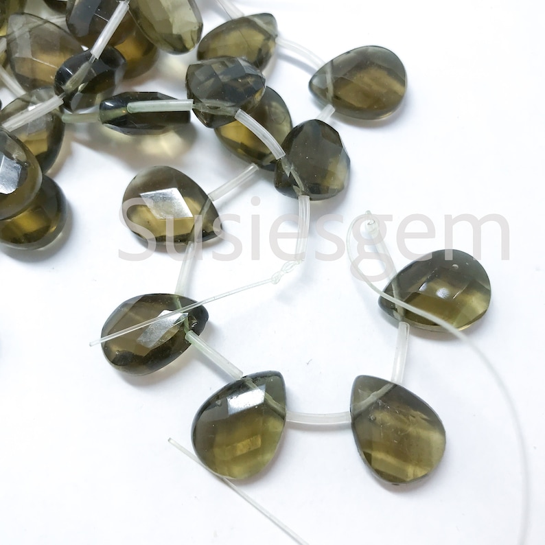 May include: A strand of dark green gemstone beads in a teardrop shape. The beads are strung on clear elastic cord.