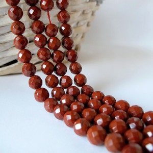 May include: A strand of red gemstone beads with a faceted finish. The beads are strung on a thin cord and are arranged in a cascading pattern.