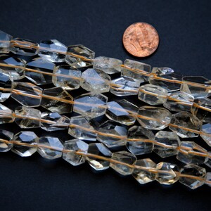 May include: A strand of faceted, clear quartz beads with a golden hue. The beads are strung on a thin wire and are approximately 1/2 inch in diameter.