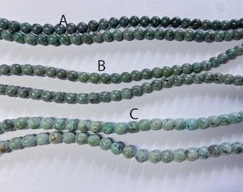 Peut inclure: Trois rangs de perles rondes et marbrées étiquetés A, B et C. Le rang A présente des tons vert forêt foncé, le rang B affiche un vert sauge moyen avec des taches noires, et le rang C se compose de perles vert menthe clair avec des inclusions.