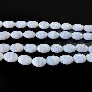 May include: Strands of oval-shaped blue lace agate beads. Each bead has a light blue base color with darker blue and white banding. The beads are strung together, ready for jewelry making. The beads are approximately 1 inch in length.