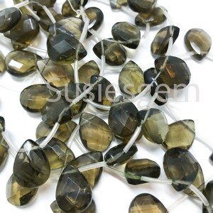 May include: A strand of faceted smoky quartz gemstone beads in a teardrop shape. The beads are strung on clear elastic cord.