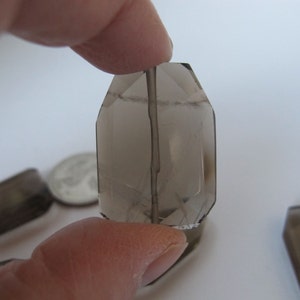 May include: A group of four smoky quartz crystal points, each with a unique shape and size. The crystals are faceted and have a translucent, smoky brown color.