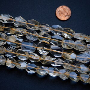 May include: A strand of faceted, translucent, light brown gemstone beads. The beads are approximately 1/2 inch in diameter and have a slightly irregular shape. The beads are strung on a clear thread and are arranged in a loose, flowing pattern.