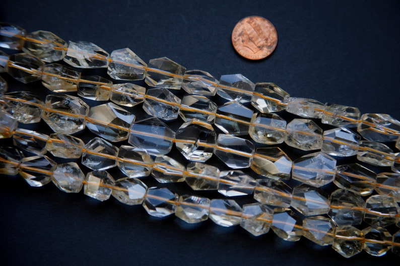 May include: A strand of faceted, translucent, light brown gemstone beads. The beads are approximately 1/2 inch in diameter and have a slightly irregular shape. The beads are strung on a clear thread and are arranged in a loose, flowing pattern.