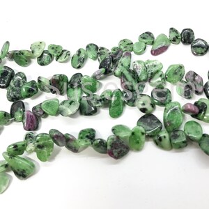 May include: A strand of green and pink gemstone beads, with a rough, tumbled finish. The beads are irregularly shaped and have a natural, earthy look.