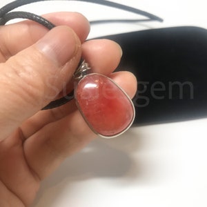 May include: A red gemstone pendant with a silver setting. The pendant is hanging from a black cord.