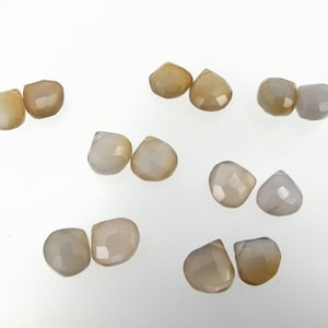 May include: A collection of ten faceted gemstone beads in shades of white and brown. The beads are teardrop shaped and have a smooth, polished finish.