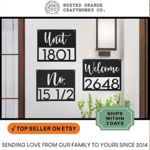 May include: Three black metal house number signs with white lettering. The signs read "Unit 1801", "No. 15 1/2", and "Welcome 2648".