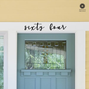 May include: A black metal wall sign featuring the words sixty four in a cursive script font, mounted horizontally above a blue door with a rectangular glass window pane. The sign is positioned on a white door frame against a yellow wall.