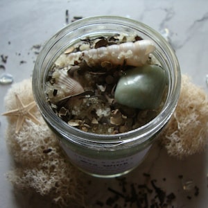 May include: A glass jar filled with bath salts, seashells, and a green stone. The jar is labeled "Sea Salt Soak".