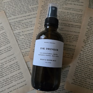 May include: A dark amber glass spray bottle with a black nozzle and a white label. The label reads WICK & CRANNY, INK DRINKER, tea-stained paper, vanilla, mahogany, leather, dusty pages, BODY & ROOM MIST, and 4 oz (118 ml) in black text.