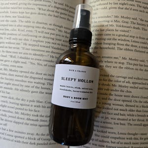 May include: An amber glass spray bottle with a black nozzle and a white label. The label reads WICK & CRANNY, SLEEPY HOLLOW, maple leaves, plum, spiced pear, woodsmoke, horse-trampled dirt, BODY & ROOM MIST, and 4 oz | 118 ml.
