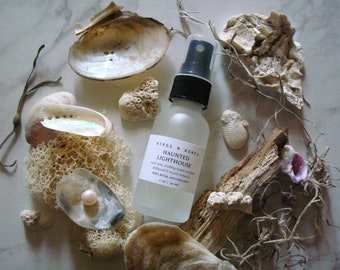 Puede incluir: Una botella de vidrio transparente con un pulverizador negro y una etiqueta blanca que dice "Birds N Bones Haunted Lighthouse room mist, creating waves, air flow diffused & mystic memories.  Bed Room and Linen Mist 4 oz | 120 ml". La botella está rodeada de conchas marinas, madera flotante y otros elementos naturales.