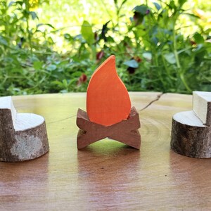 May include: A set of three wooden toy furniture pieces, including two brown and white log chairs and a small orange flame on a brown log base.