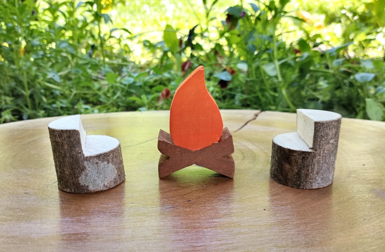 May include: A set of three wooden toy furniture pieces, including two brown and white log chairs and a small orange flame on a brown log base.
