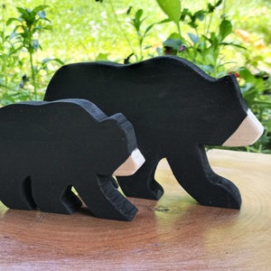 May include: Two black wooden bear figurines, one larger than the other, with white accents on their faces. The bears are standing on a wooden surface.