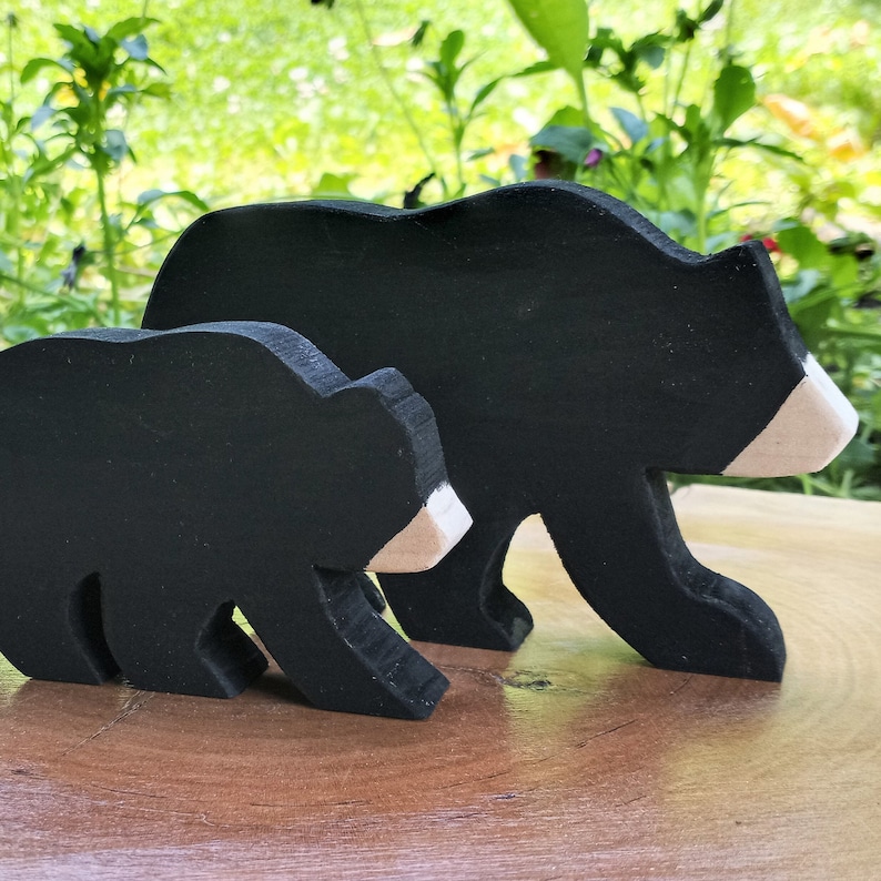 May include: Two black wooden bear figurines, one larger than the other, with white accents on their faces. The bears are standing on a wooden surface.