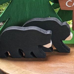 May include: Two black wooden bear figurines with white accents. The bears are standing on a wooden surface.