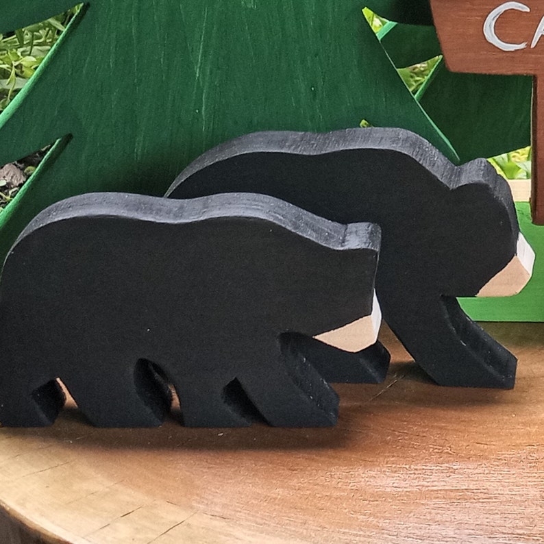 May include: Two black wooden bear figurines with white accents. The bears are standing on a wooden surface.
