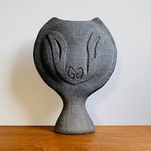 May include: A black ceramic sculpture of a stylized face with a rounded, bowl-like top and a slender base.
