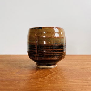 May include: A brown and black ceramic cup with a textured surface and a glossy finish. The cup has a wide base and a rounded shape.