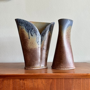 May include: Two ceramic vases with a brown and blue glaze. The larger vase has a wide, open mouth and a narrow base. The smaller vase is tall and slender. Both vases have a textured surface.