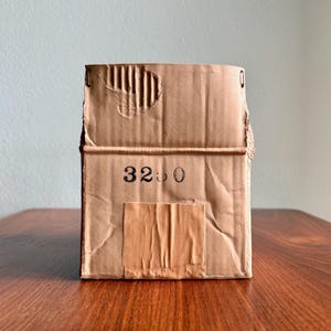 May include: A rectangular cardboard box with a worn, textured surface. The box has a torn top and a small, rectangular patch of tape. The number "3250" is printed on the front of the box in black ink.
