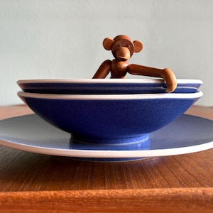 May include: A blue ceramic bowl and saucer set with a white rim, and a wooden monkey figurine. The monkey is brown and has articulated limbs. The bowl is approximately 6 inches in diameter.