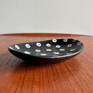 May include: A black ceramic dish with a shallow, oval shape. The dish is decorated with white and teal-colored polka dots. The dish is sitting on a wooden surface.