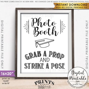 May include: A framed digital printable sign with the words "Photo Booth" in a decorative font, a graduation cap illustration, and the phrase "Grab a Prop and Strike a Pose." The sign is white with black text and a brown frame.