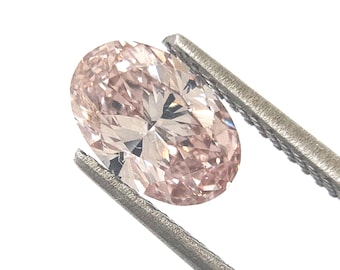 May include: An oval-cut loose gemstone with a pale pink hue and a faceted surface that reflects light. The stone is held by a pair of silver-toned metal tweezers, showcasing its translucent quality and symmetrical shape against a plain white background.